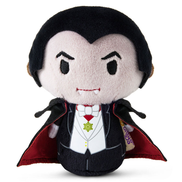A plush vampire doll with black hair, a pale face, a black tuxedo, white shirt, red cape lining, and small vampire fangs, photographed on a plain white background.