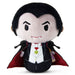 A plush vampire doll with black hair, a pale face, a black tuxedo, white shirt, red cape lining, and small vampire fangs, photographed on a plain white background.