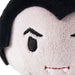 Close-up of a plush toy face with pale pink fabric, black embroidered eyes and hair, and small white fangs with red stitched detail.