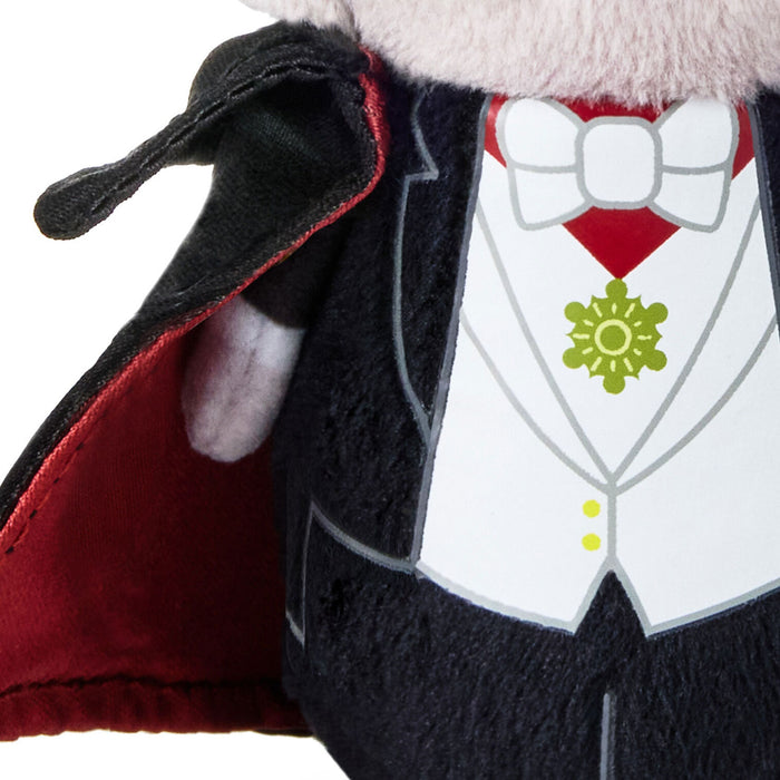 Close-up of a plush vampire costume or doll torso with a black cape, white tuxedo-style vest, red inner lining, white bow tie, and a green flower emblem on a white background.