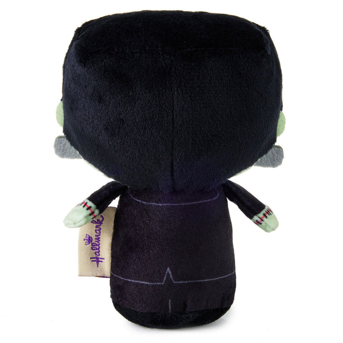 A plush toy shown from the back, featuring a large black head, a dark purple body with stitched details, light green hands, and a visible Harrowman tag on the left side, set against a plain white background.