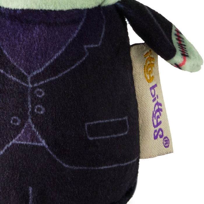 Close-up of a plush toy wearing a dark purple vest, with a beige fabric tag on the side that reads 'Bugs' in purple and yellow.