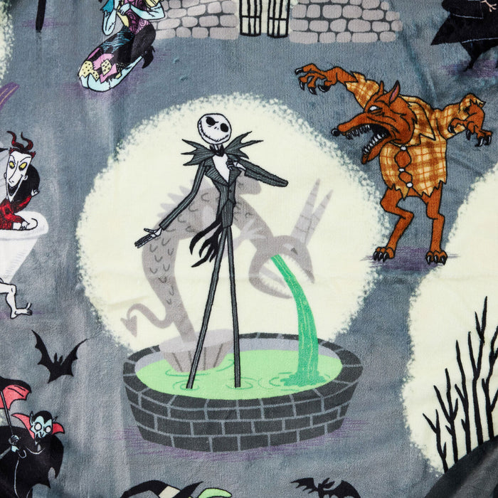 A close-up of a printed fabric featuring characters from The Nightmare Before Christmas, including Jack Skellington in a black suit standing in a green pool, a brown three-headed dog, and other spooky motifs on a muted blue-gray background.
