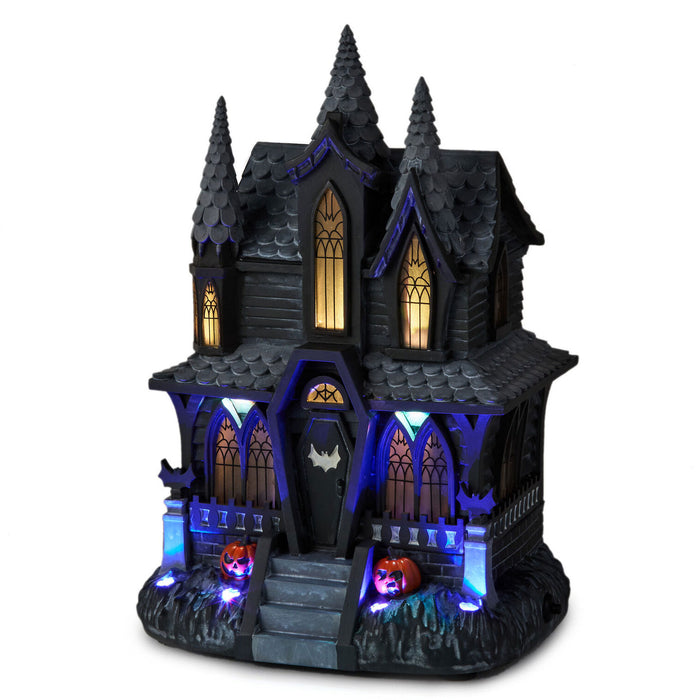 A gothic haunted house Halloween decoration with illuminated windows, blue LED lighting accents, and jack-o'-lanterns on a white background.