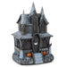 A dark gray plastic haunted house Halloween decoration with pointed spires, arched windows, a bat-shaped door emblem, gray faux-ice detailing on the base, and two small orange jack-o'-lanterns on the front, shown on a plain white background.