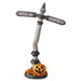 Halloween decorative signpost with two directional arrows reading 'WITCH WAY' and 'HAUNTED DR', topped with a small skull, mounted on a round base with a carved pumpkin and autumn leaves, shown on a white background.