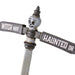 A Halloween street sign decoration featuring a weathered metal T-post with a skull ornament on top, one arm reading 'WITCH WAY' and the other 'HAUNTED DR' in white text on a distressed gray and off-white background.