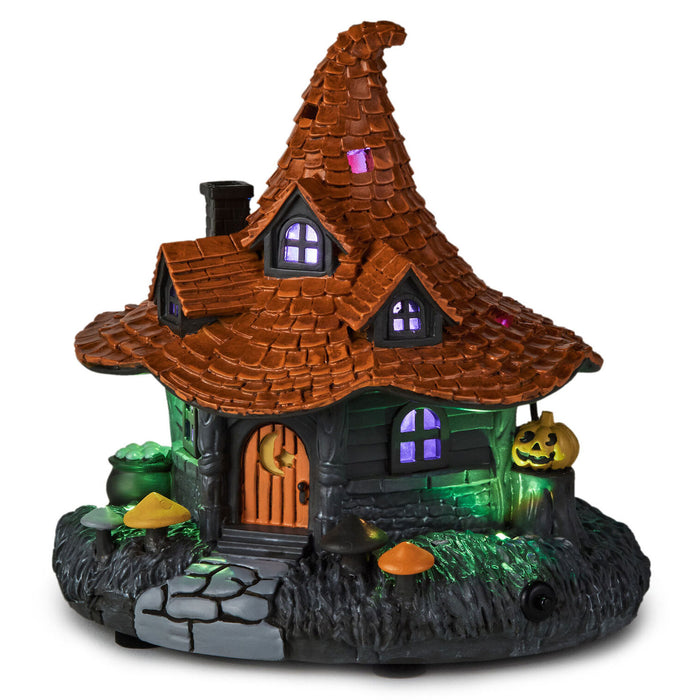 A decorative miniature haunted house Halloween ornament with a pointed orange-brown roof, glowing purple windows, an orange door, green-lit base, cauldron, mushrooms, and a jack-o'-lantern on a white background.