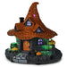 A decorative miniature haunted house Halloween ornament with a pointed orange-brown roof, glowing purple windows, an orange door, green-lit base, cauldron, mushrooms, and a jack-o'-lantern on a white background.