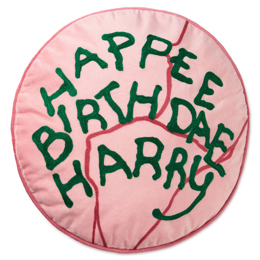 A round pink cushion with embroidered green text reading 'HAPPEE BIRTHDAE HARRY' on a white background.