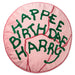 A round pink cushion with embroidered green text reading 'HAPPEE BIRTHDAE HARRY' on a white background.