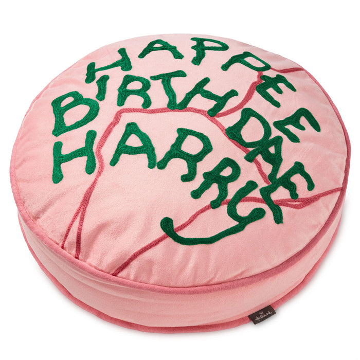 A round pink plush cushion with green embroidered text reading 'HAPPY BIRTH HARRICTON' and red stitched crack details, shown on a white background.