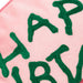 A close-up of a pink knit fabric with large green letters spelling part of a word, showing the texture of the yarn.