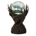A decorative tabletop sculpture featuring a dark brown tree trunk base with branching arms holding a clear glass globe. Inside the globe is a light blue vintage car surrounded by green leaf-like confetti.