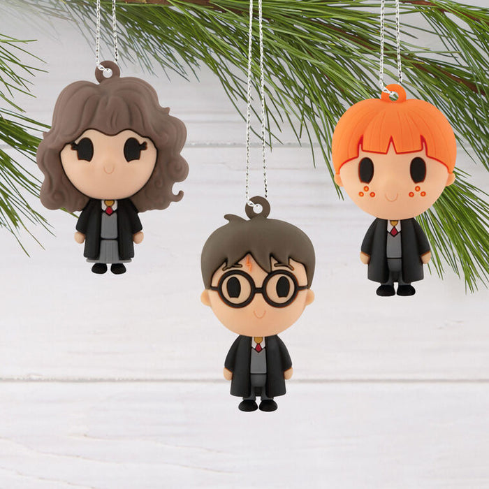 Three small hanging character ornaments shaped like Harry Potter characters are displayed against a white wood background with green pine branches at the top.