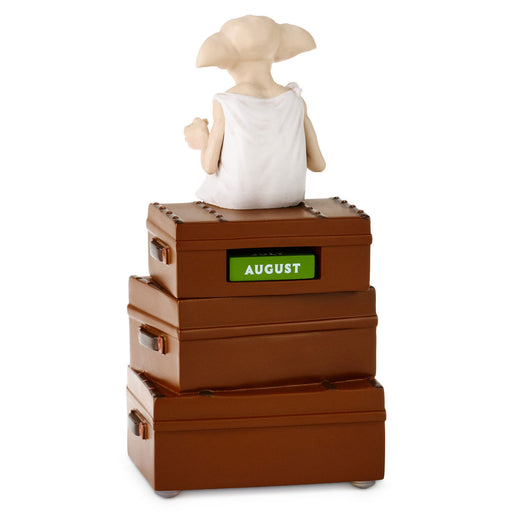 A collectible figurine of Dory from Finding Nemo sitting on top of three stacked brown storage boxes. The middle box features a green label with the word 'AUGUST' in white.