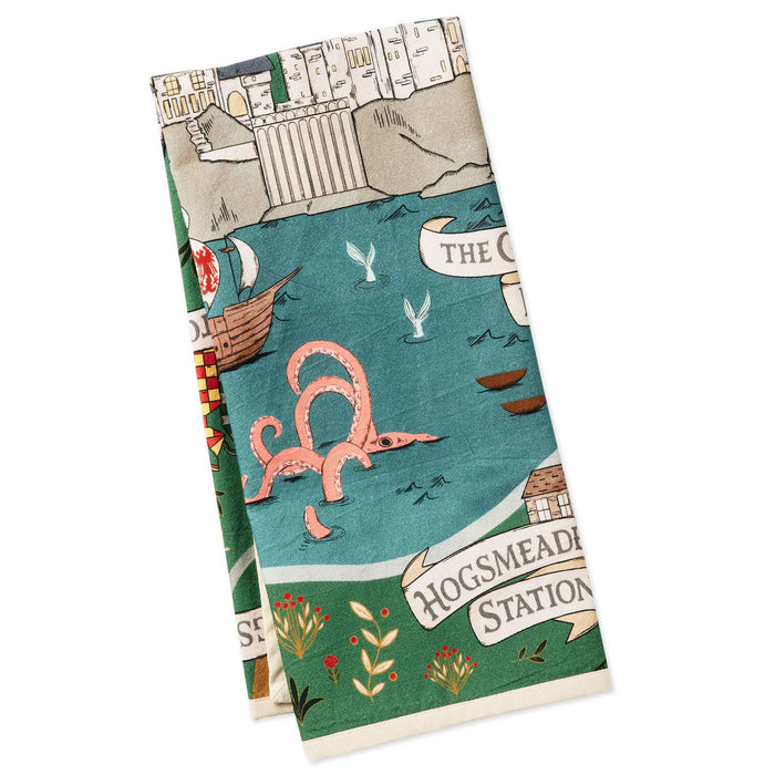 A folded tea towel featuring a whimsical illustrated map design with a pink octopus, a boat, buildings, and text reading 'HOGSMEADEN STATION' and 'THE C.