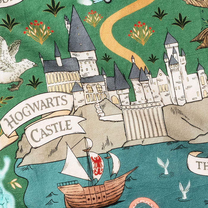 A close-up of a printed fabric featuring Hogwarts Castle from Harry Potter, with a green background, blue water, a boat, birds, plants, and banners reading 'HOGWARTS CASTLE'.