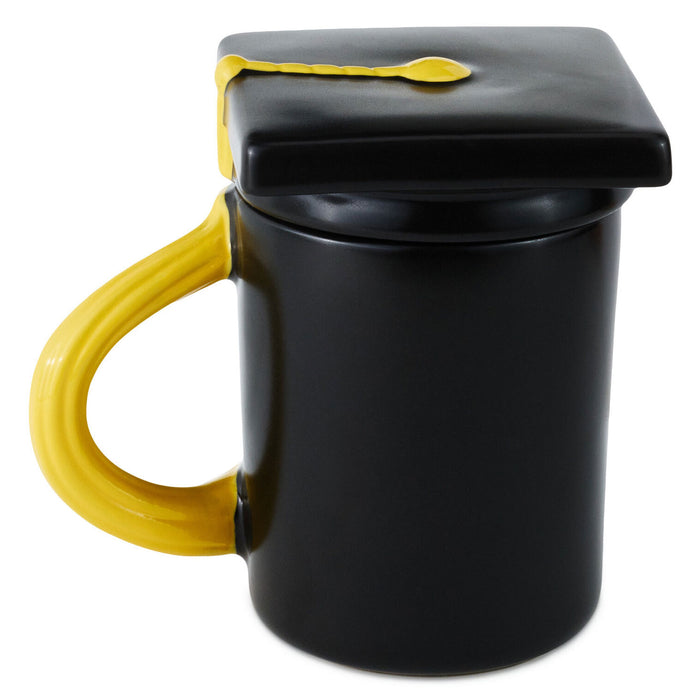 Black mug with yellow handle and graduation cap lid on a white background