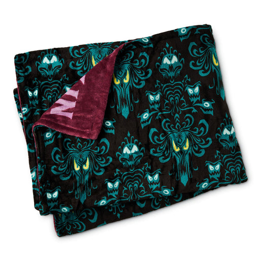 A folded throw blanket with a black background, teal gothic damask pattern featuring ghostly faces and owl motifs, and a plush burgundy reverse side with a pink letter.