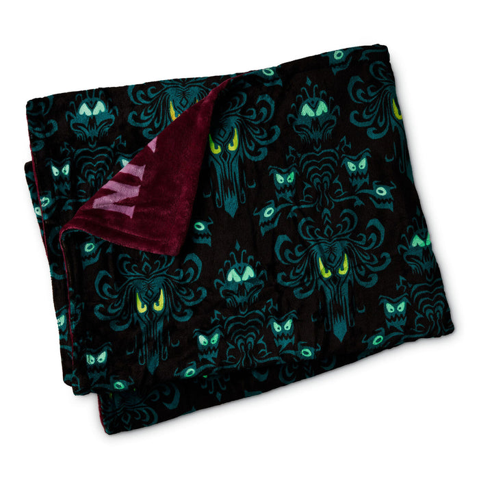 A folded plush blanket with a black background, teal gothic damask patterns, and green owl faces, showing a burgundy sherpa lining on one side.