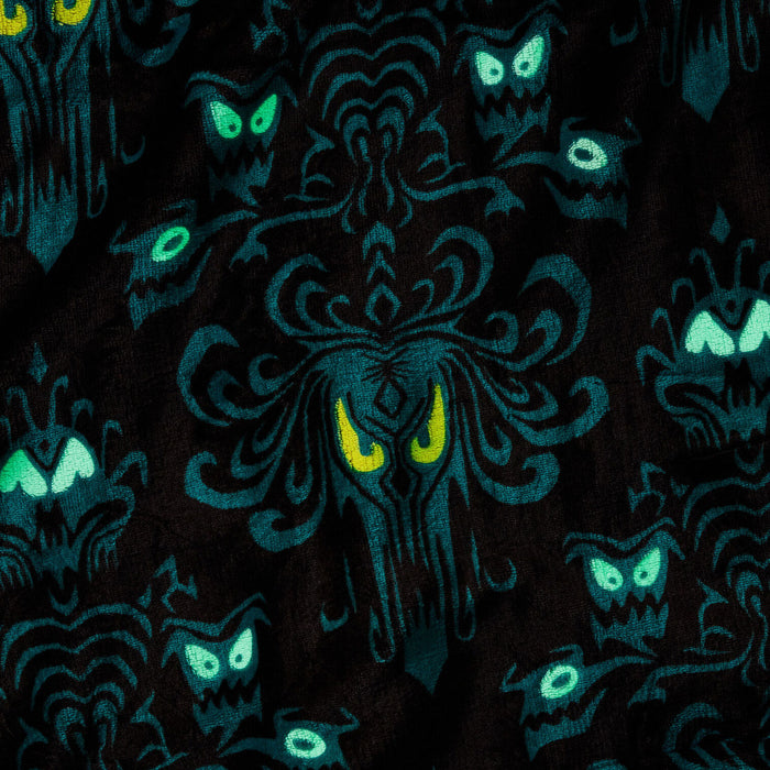 A close-up of a black fabric with a repeating gothic pattern featuring dark teal ornate motifs and glowing green and yellow eyes.