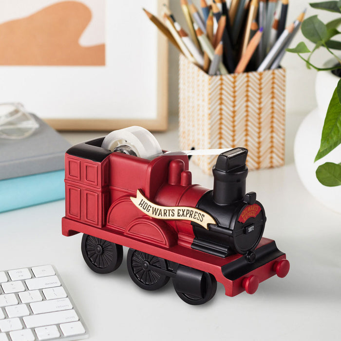 Red train-shaped tape dispenser on a desk with stationery items in the background