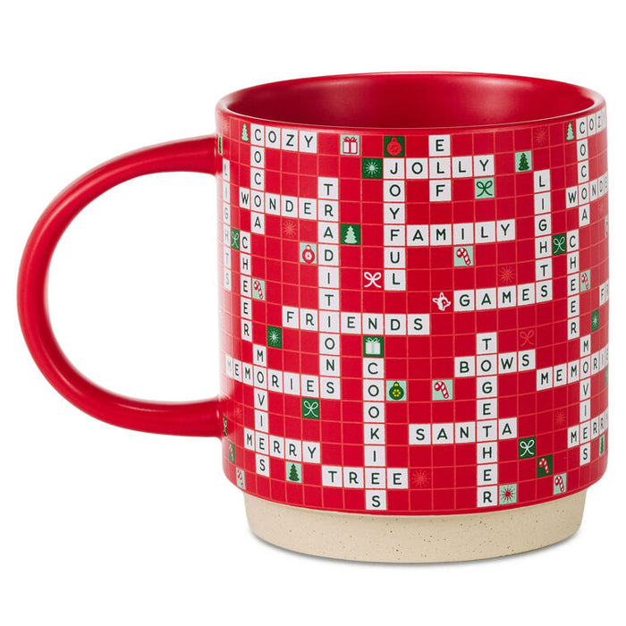 A red ceramic mug featuring a Scrabble-themed holiday design with white and green tiles spelling out Christmas words on a red grid background, set against a plain white studio background.