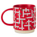 A red ceramic mug featuring a Scrabble-themed holiday design with white and green tiles spelling out Christmas words on a red grid background, set against a plain white studio background.