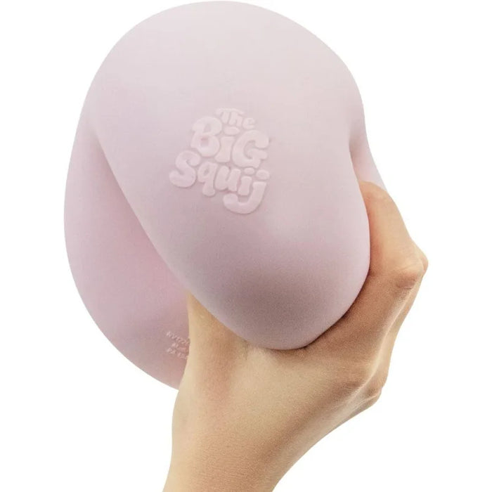 A hand holding a large, soft, light pink silicone squishy toy with the embossed brand name 'The Big Squj' visible on its surface, set against a plain white background.