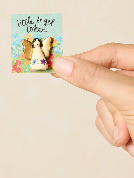 Hand holding a small angel token with a colorful card featuring flowers and text.