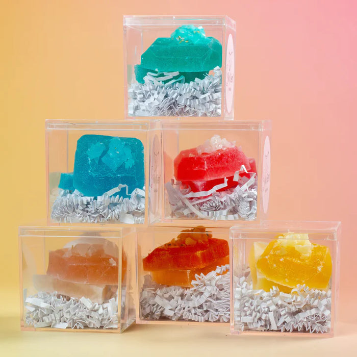 Stack of transparent boxes containing colorful soap bars on a gradient background