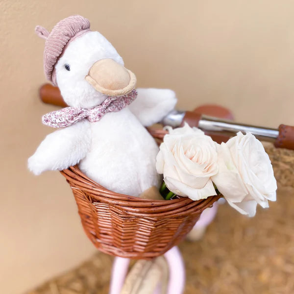 White plush duck with a pink hat and scarf in a wicker basket with white roses on a blurred background