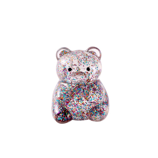 A small teddy bear figurine covered in dense multicolor glitter, featuring a sad expression and small circular ears, shown on a plain white background.