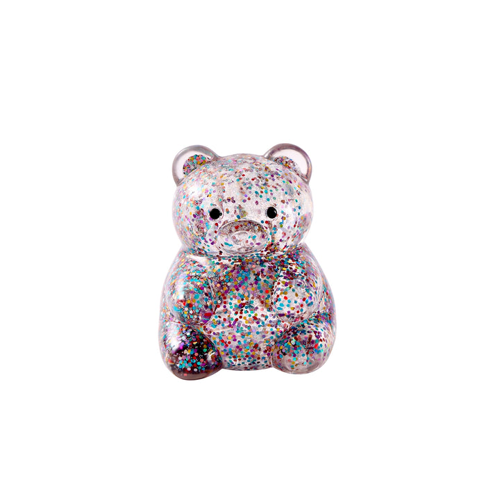 A small teddy bear figurine covered in dense multicolor glitter, featuring a sad expression and small circular ears, shown on a plain white background.