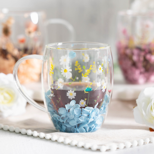 Clear mug with floral design filled with a dark liquid, placed on a white surface with blurred background.