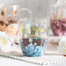 Clear mug with floral design filled with a dark liquid, placed on a white surface with blurred background.