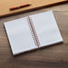 Open notebook with spiral binding on a wooden surface, accompanied by a pen.