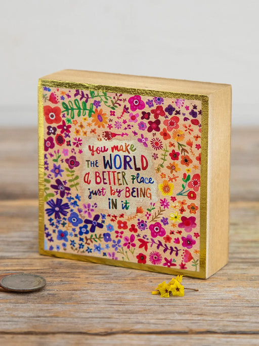Decorative wooden block with floral design and motivational quote on a wooden surface.