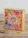 Decorative wooden block with floral design and motivational quote on a wooden surface.