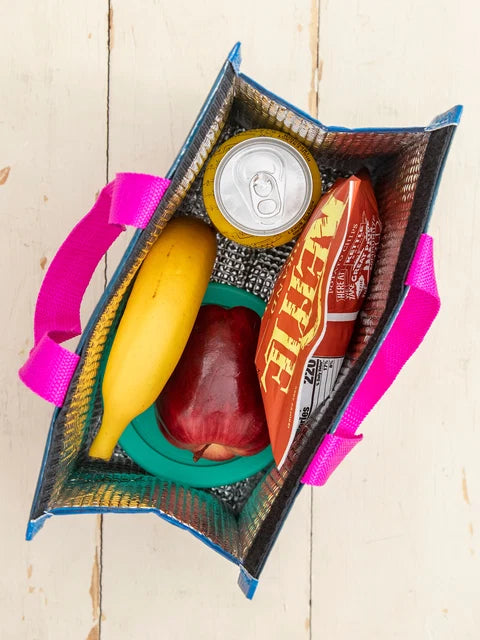 Reusable shopping bag with a banana, apple, can of soda, and bottle of hot sauce on a wooden surface.