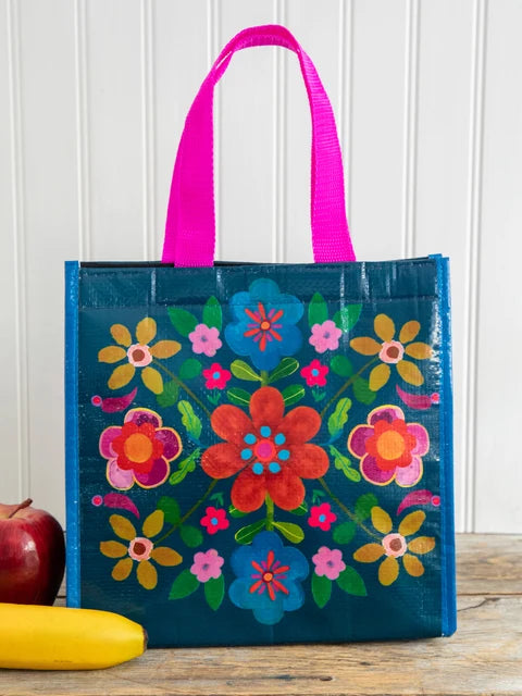 Colorful floral-patterned tote bag with pink handles on a wooden surface.