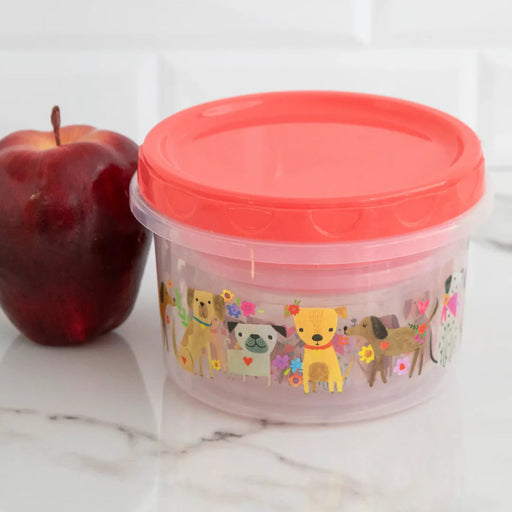 Container with a red lid and animal design next to an apple on a white surface