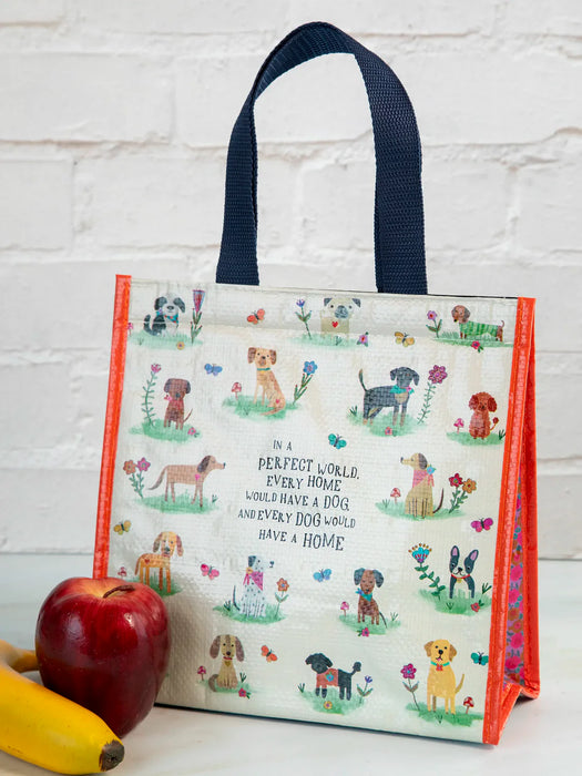 Reusable shopping bag with dog illustrations and text, next to an apple and banana on a white surface.