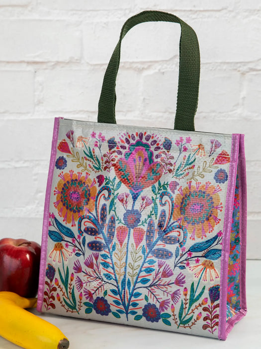 Colorful floral-patterned bag with green handles on a white brick wall background