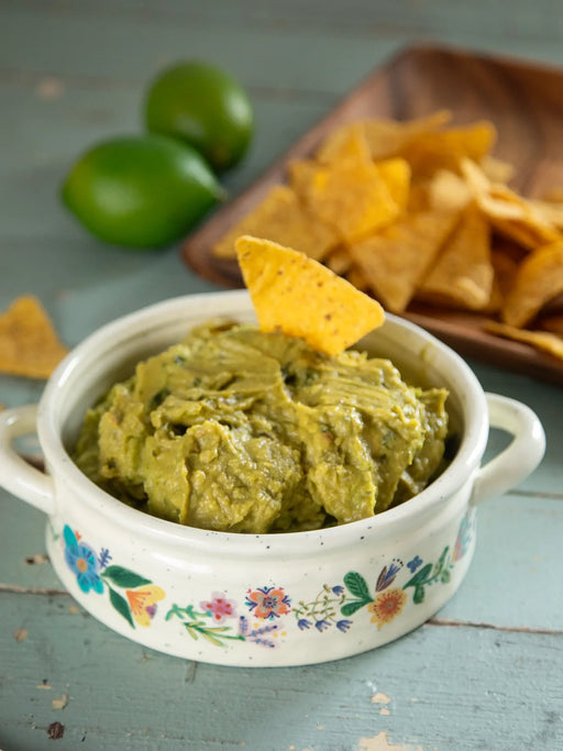 Guacamole in a decorative bowl with a tortilla chip on a wooden surface