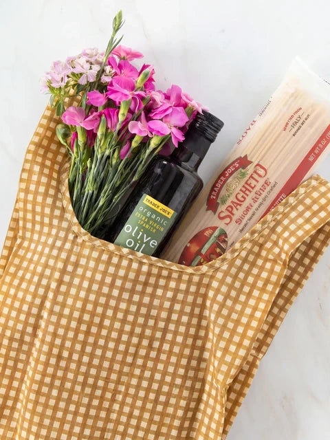 Yellow checkered apron with a bouquet of pink flowers, bottle of olive oil, and box of Spaghetti.