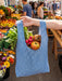 Blue checkered bag filled with fresh produce held in front of a market scene.