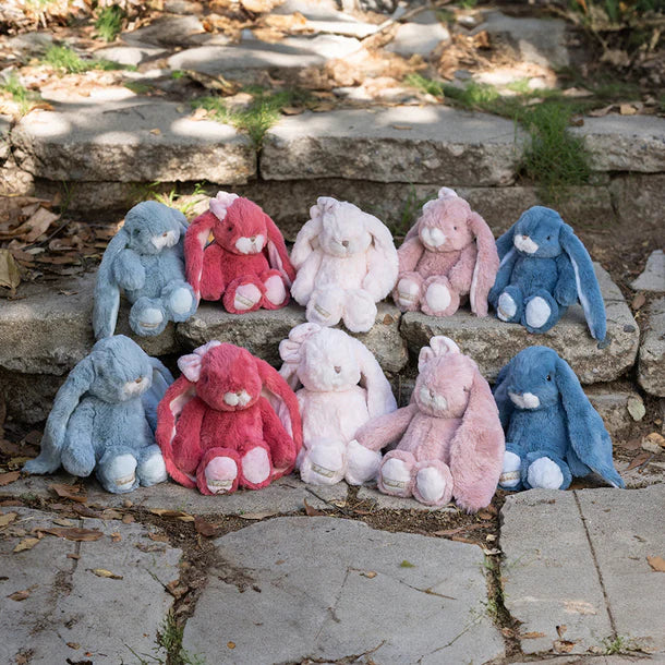 Plush bunny toys in various colors sitting on stone steps outdoors.