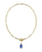 A gold paperclip chain necklace with a toggle clasp and a small oval blue gemstone pendant, shown on a plain white background.